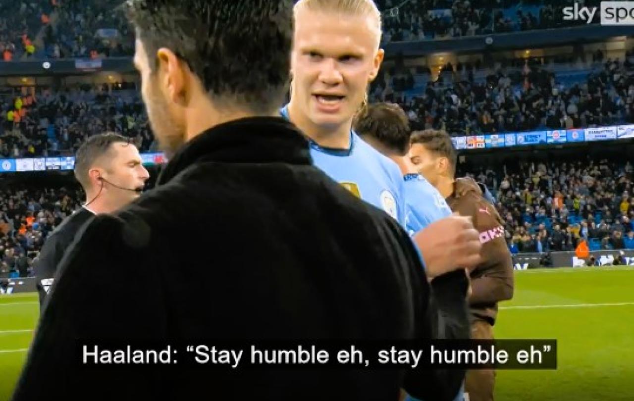 A TV screengrab shows a football manager walking while a passing rival player says (captioned) 'stay humble'.