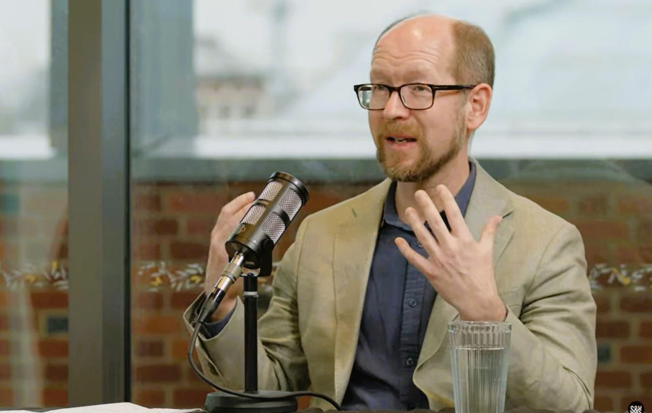 A podcast guest sits in front of a mic, gesturing with their hands.