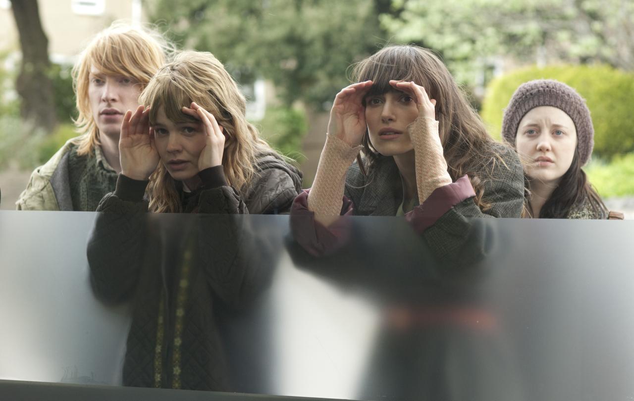 Four young people peer through a window.