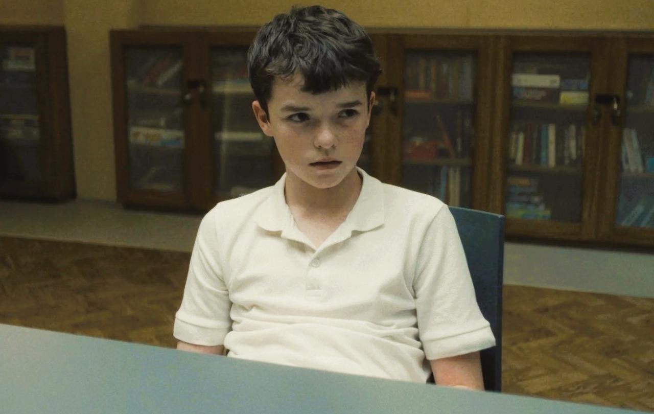 A worried looking adolescent boy slumped in a chair looks up.