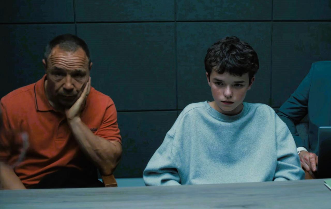 An unhappy father sits next to a scared son in a police interview room.