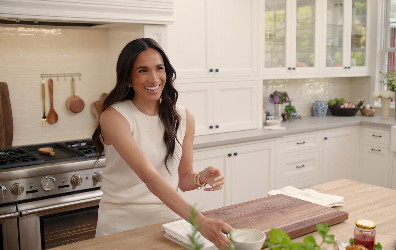 A woman stands at a kitchen island with a chopping board on it.