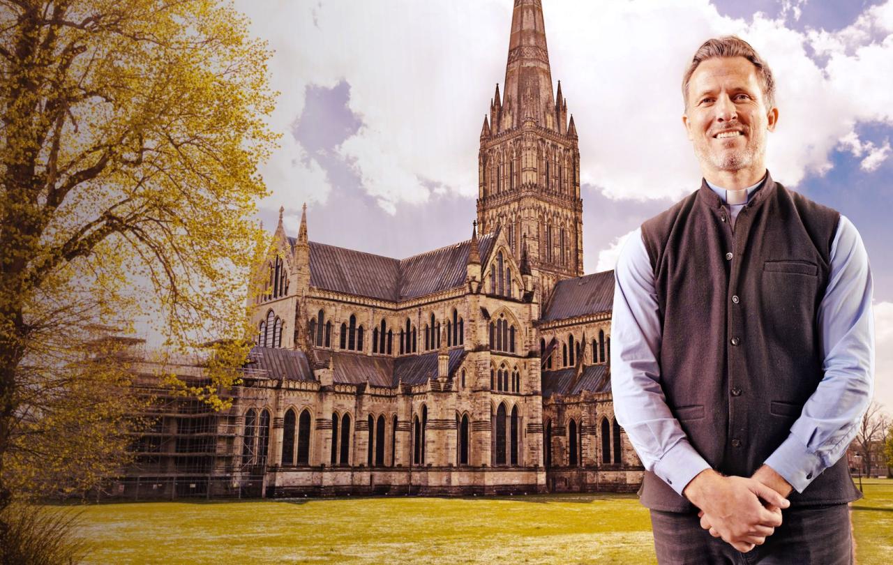 A vicar stands arms in front of himself, behind him is a cathedral