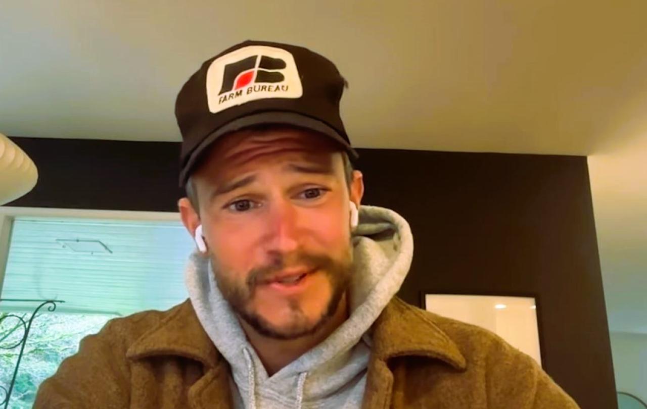 A podcast guest, wearing a baseball hat, looks at a screen.