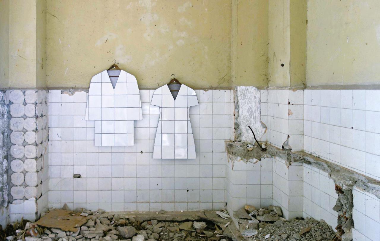 In a bombed-out tiled room, two art works hang in the shape of a tiled jacket and shape