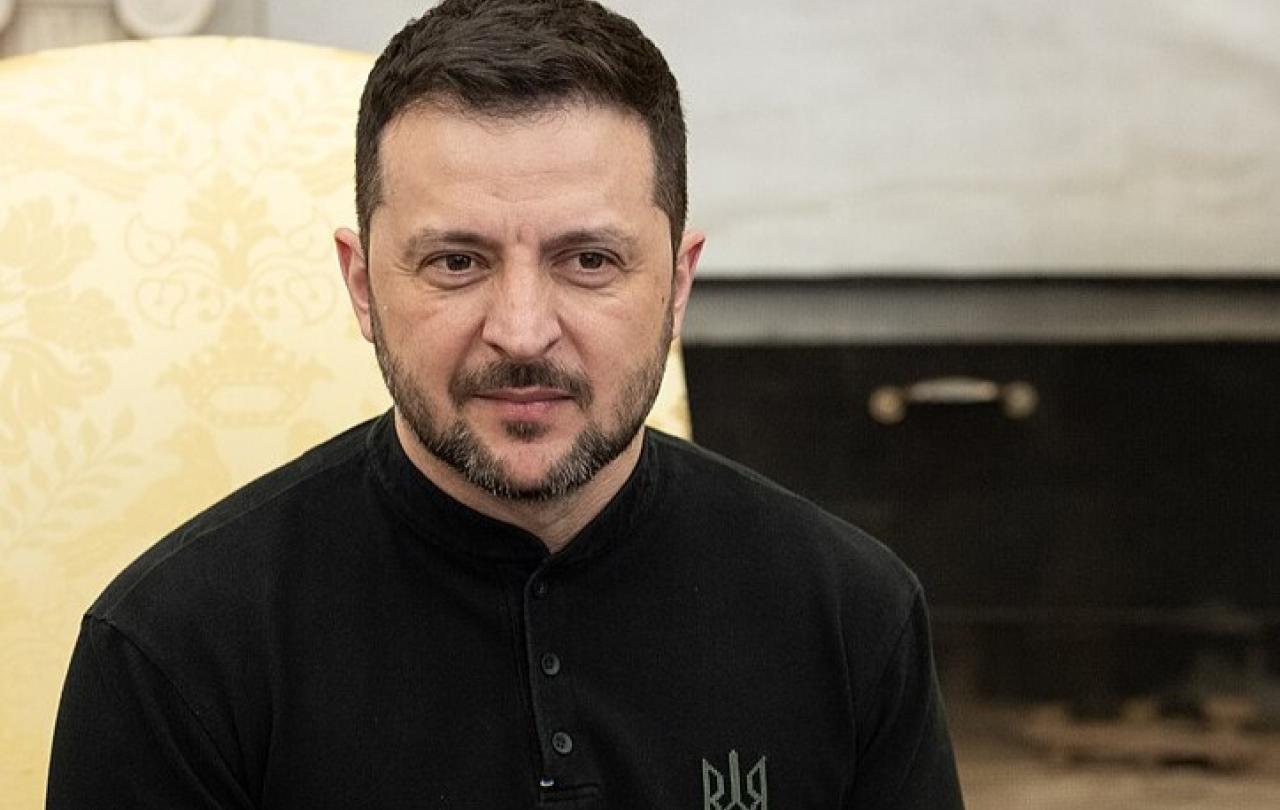 President Zelensky, wearing black, sits silently.