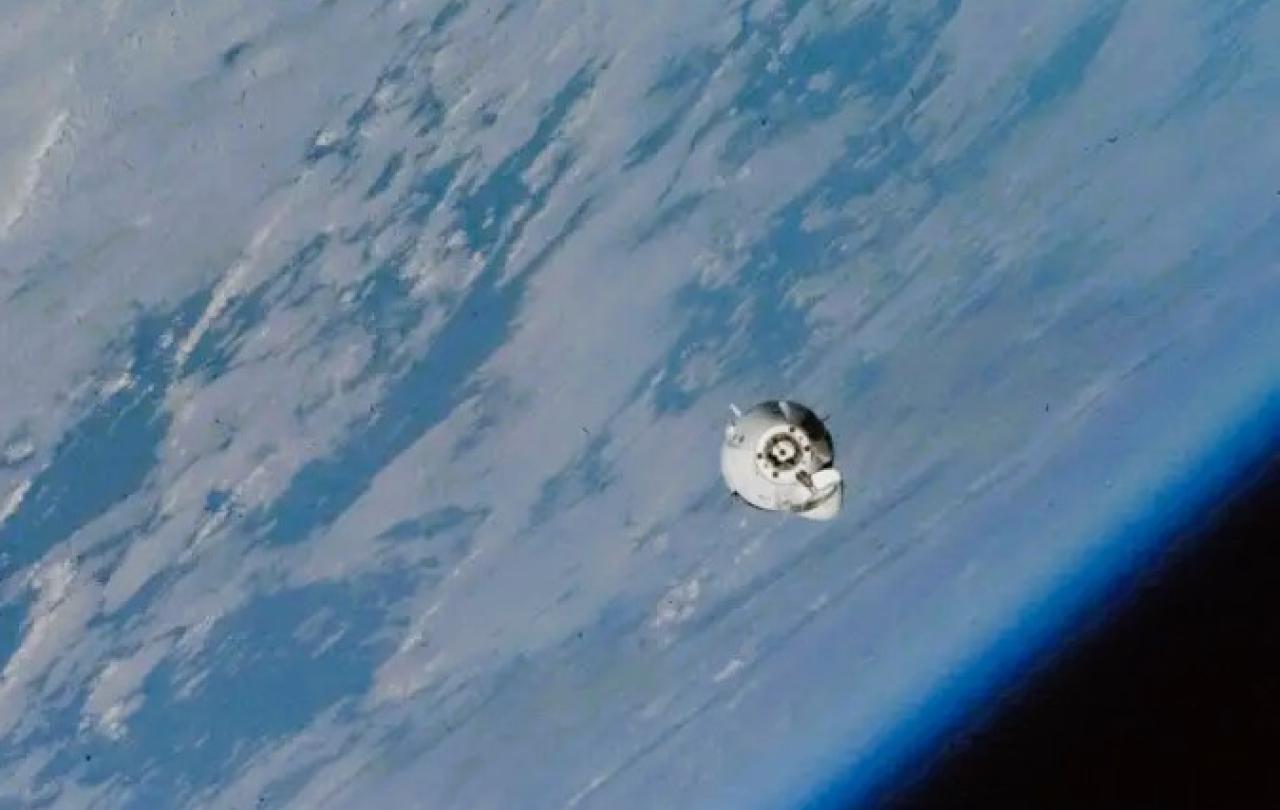 A small white space capsule orbits around the earth.