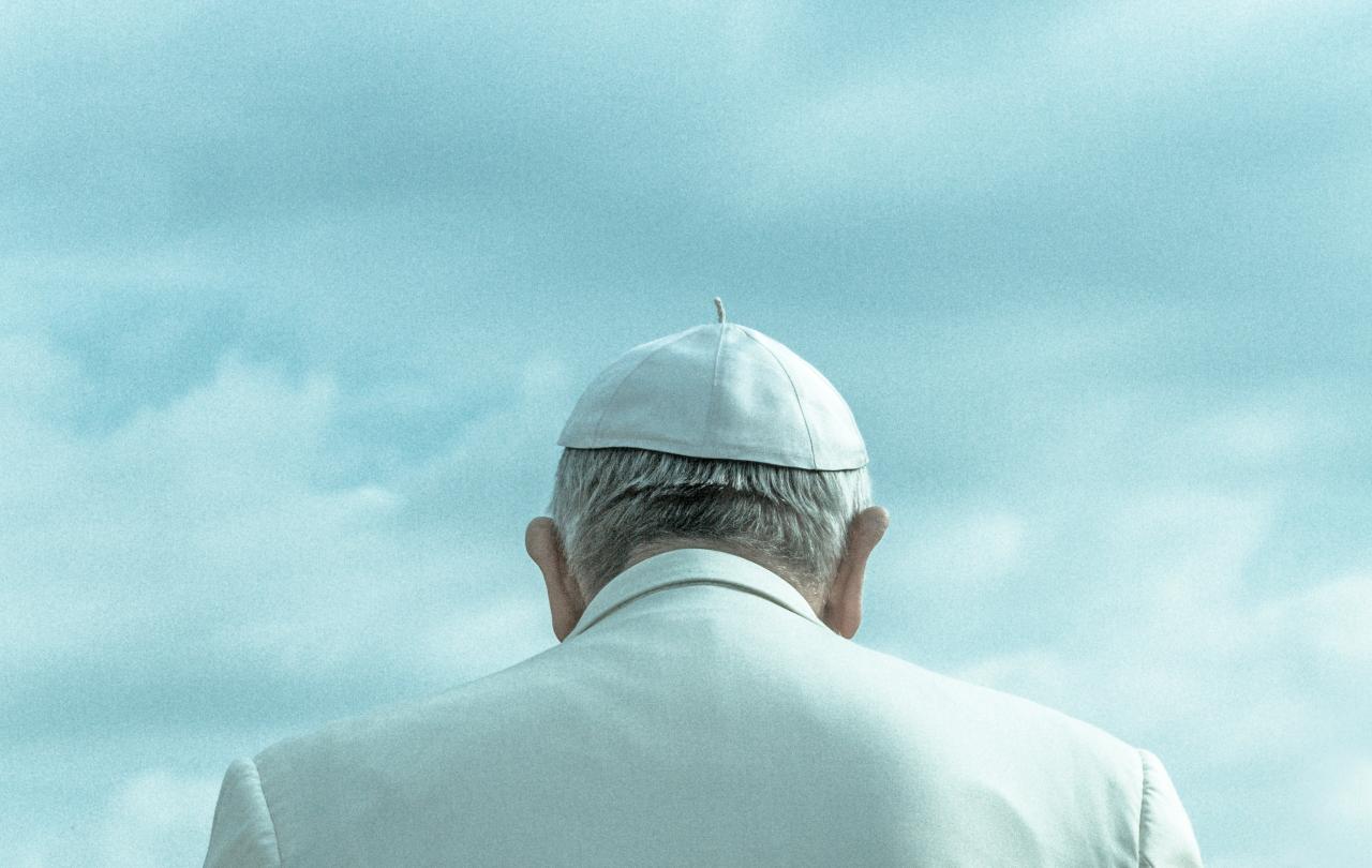 A pope wearing a white skull cap and white robe, viewed from behind