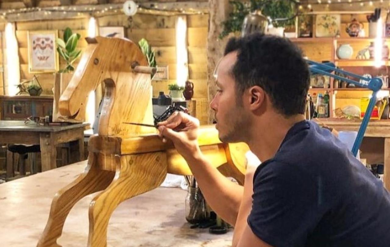 A restorer rest on his elbows while painting a wooden rocking horse.