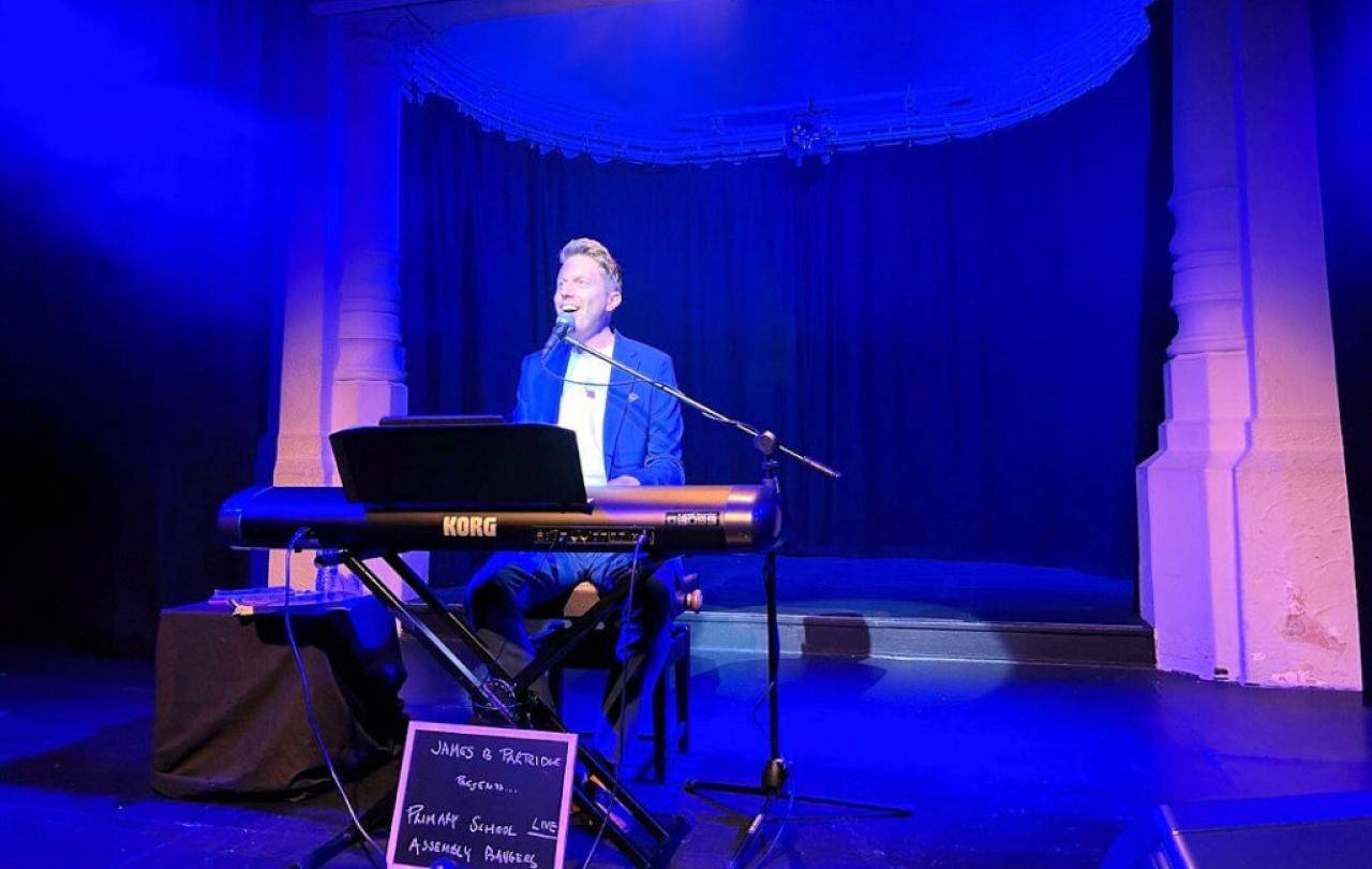 A pianist sits at a keyboard singing on a stage.