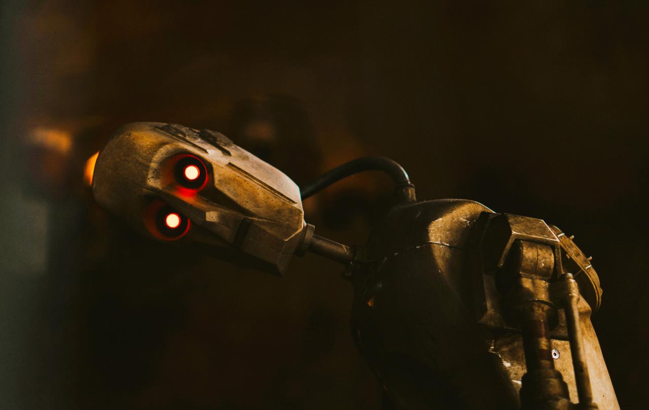 A tarnished humaniod robot rests its head to the side, its LED eyes look to the camera.