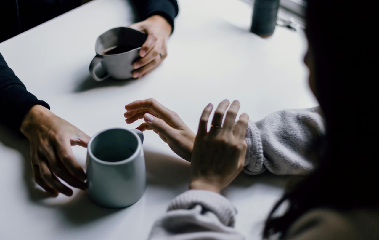 A cup of coffee is offered across a table to a hand that is hesitant.