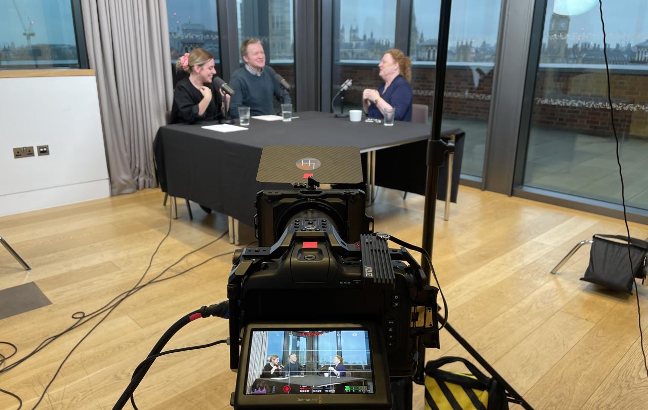 A camera's screen shows a podcast recording also visible in the background.