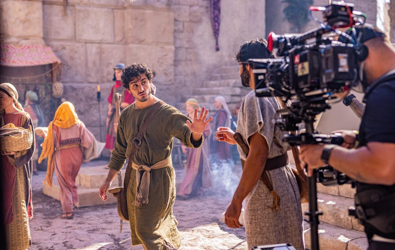An actor dressed in an ancient Middle Eastern way is filmed by a large camera.
