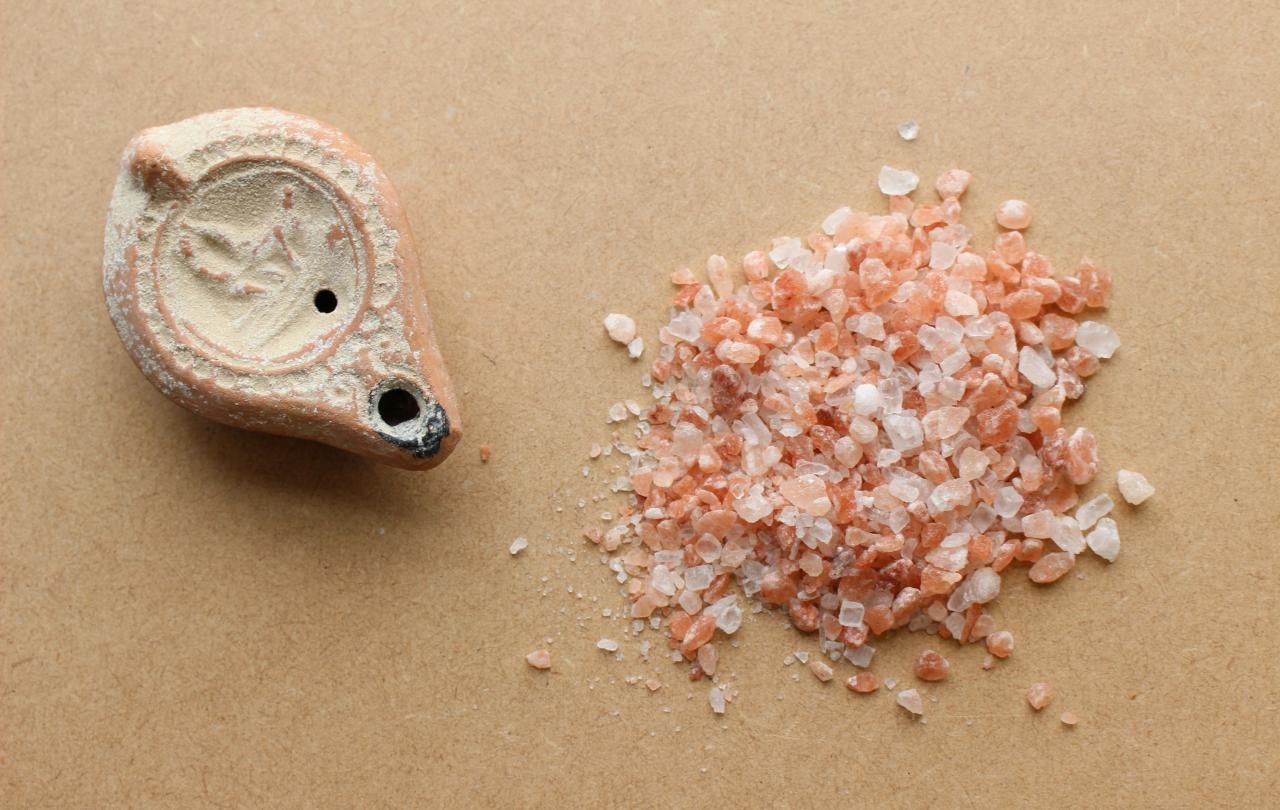 An ancient salt shaker sits next to a pile of crushed rock salt.