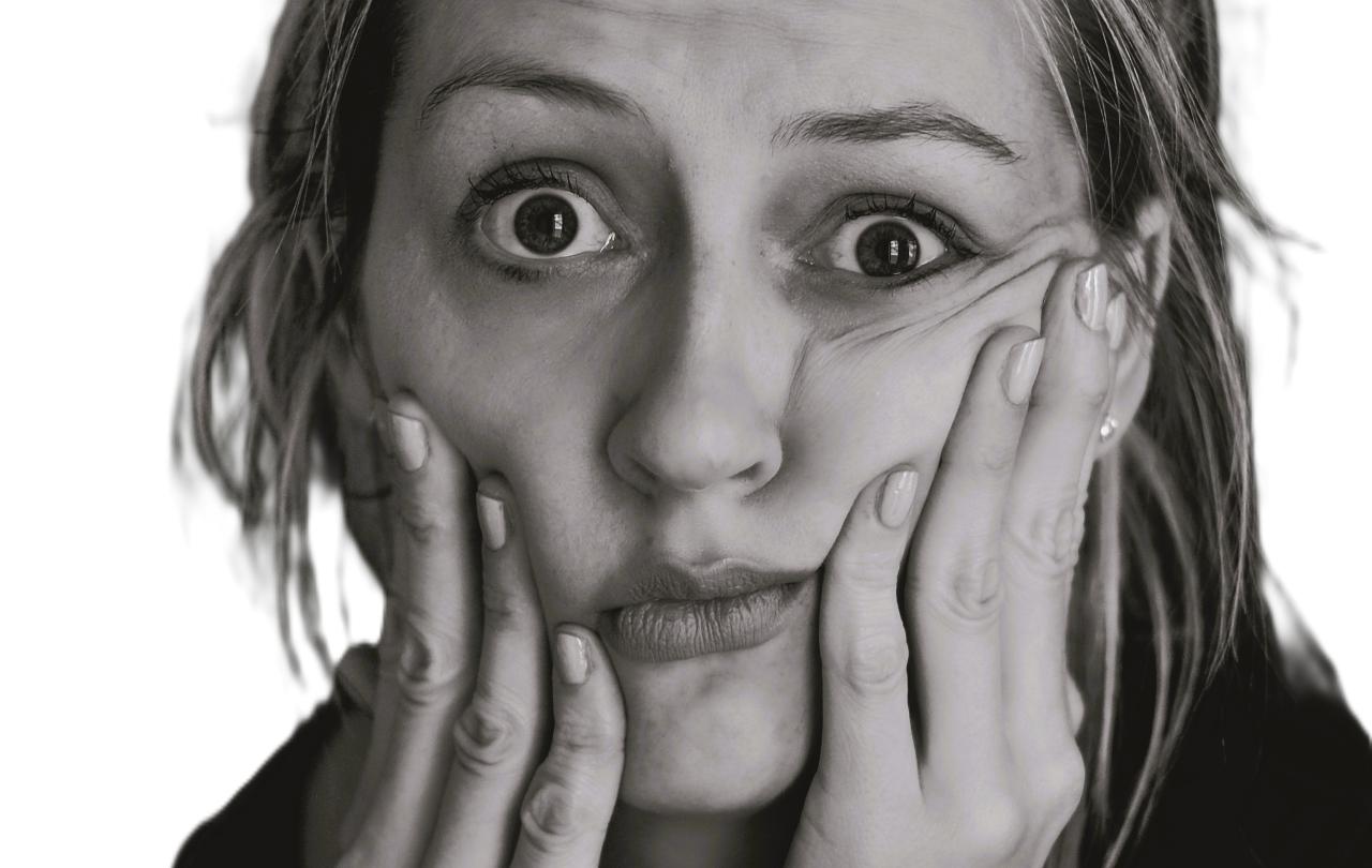 A perplexed looking woman hold her cheeks up with her fingers.