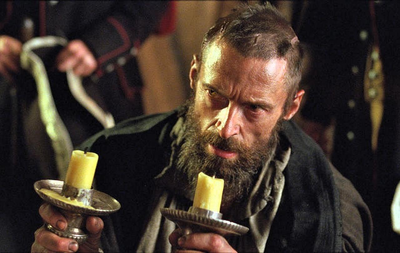 A desperate man wearing 18th century clothes holds candlesticks