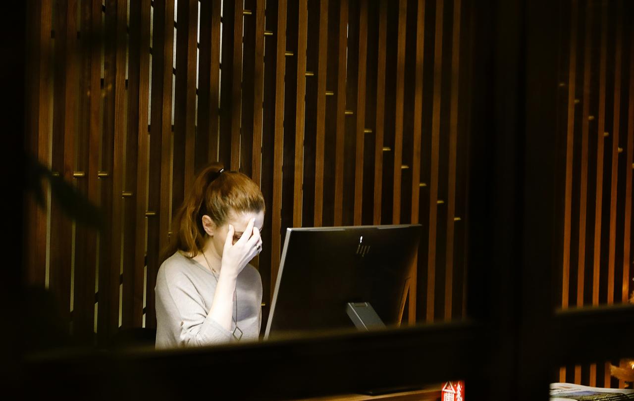 A woman rubs her face in worry, while siting at a screen.