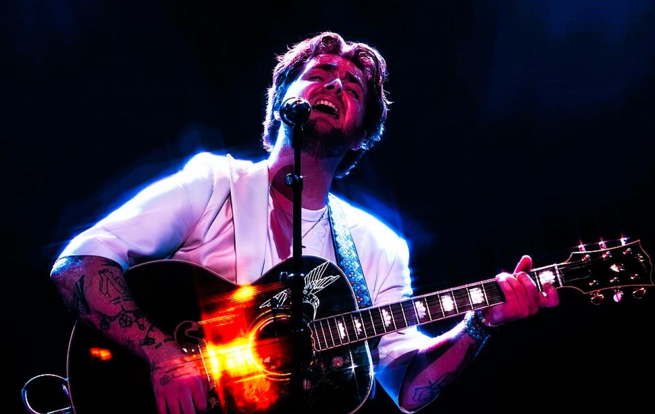 A singer holding a guitar raises his head with closed eyes.