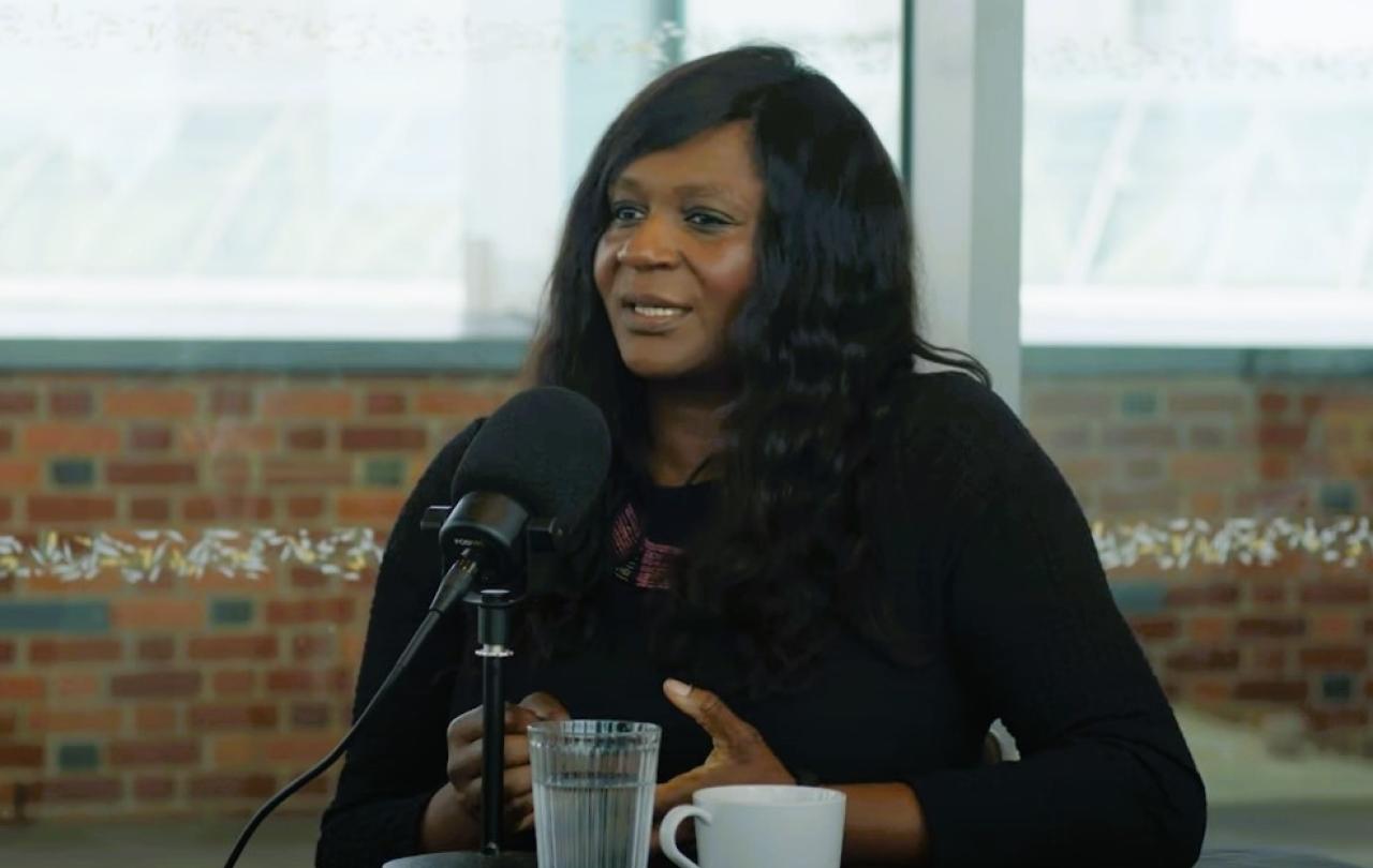 A podcast guest sits in front of a mic talking and gesturing with her hands.
