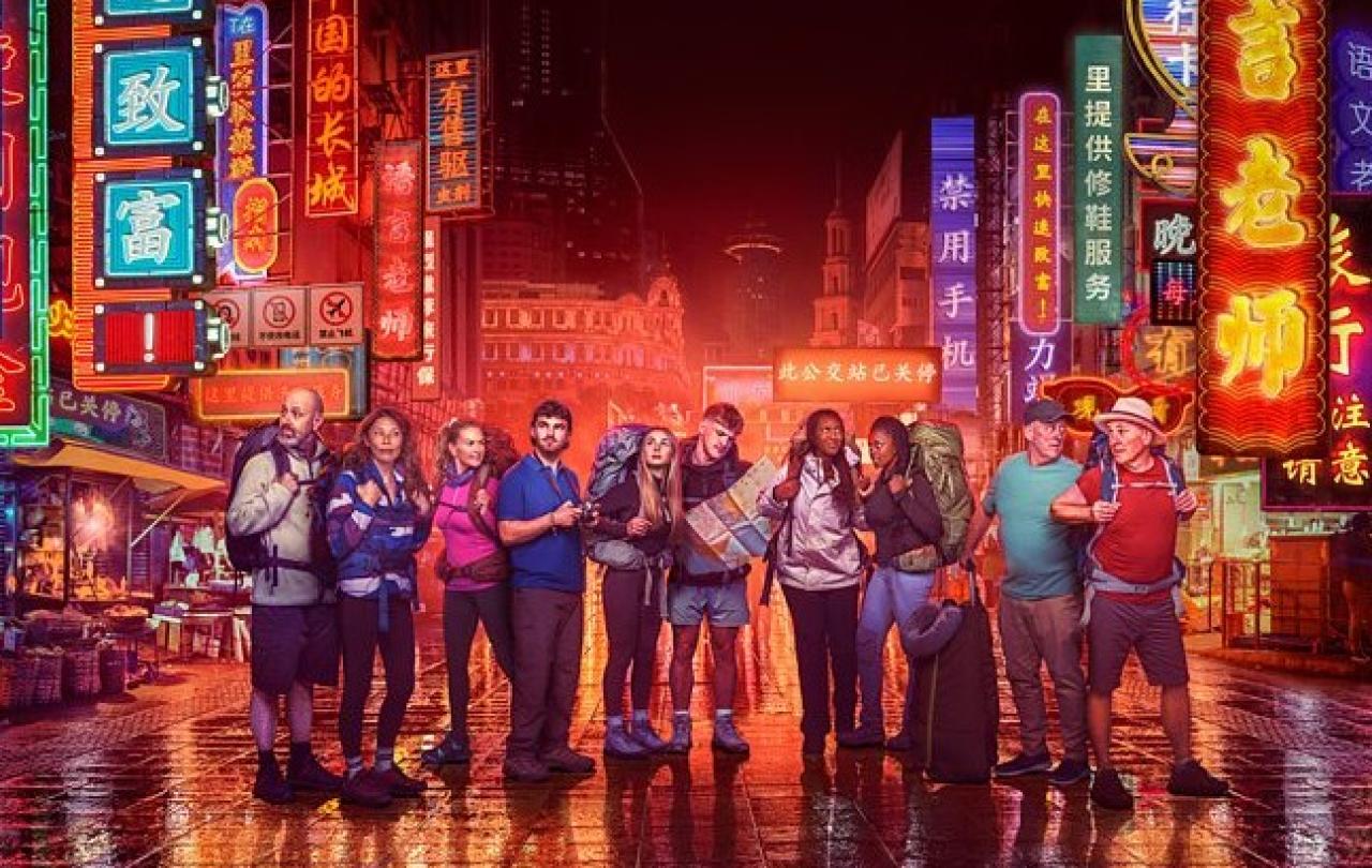 Contestants in Race Across the world stand in front of neon-lit Chinese street scene