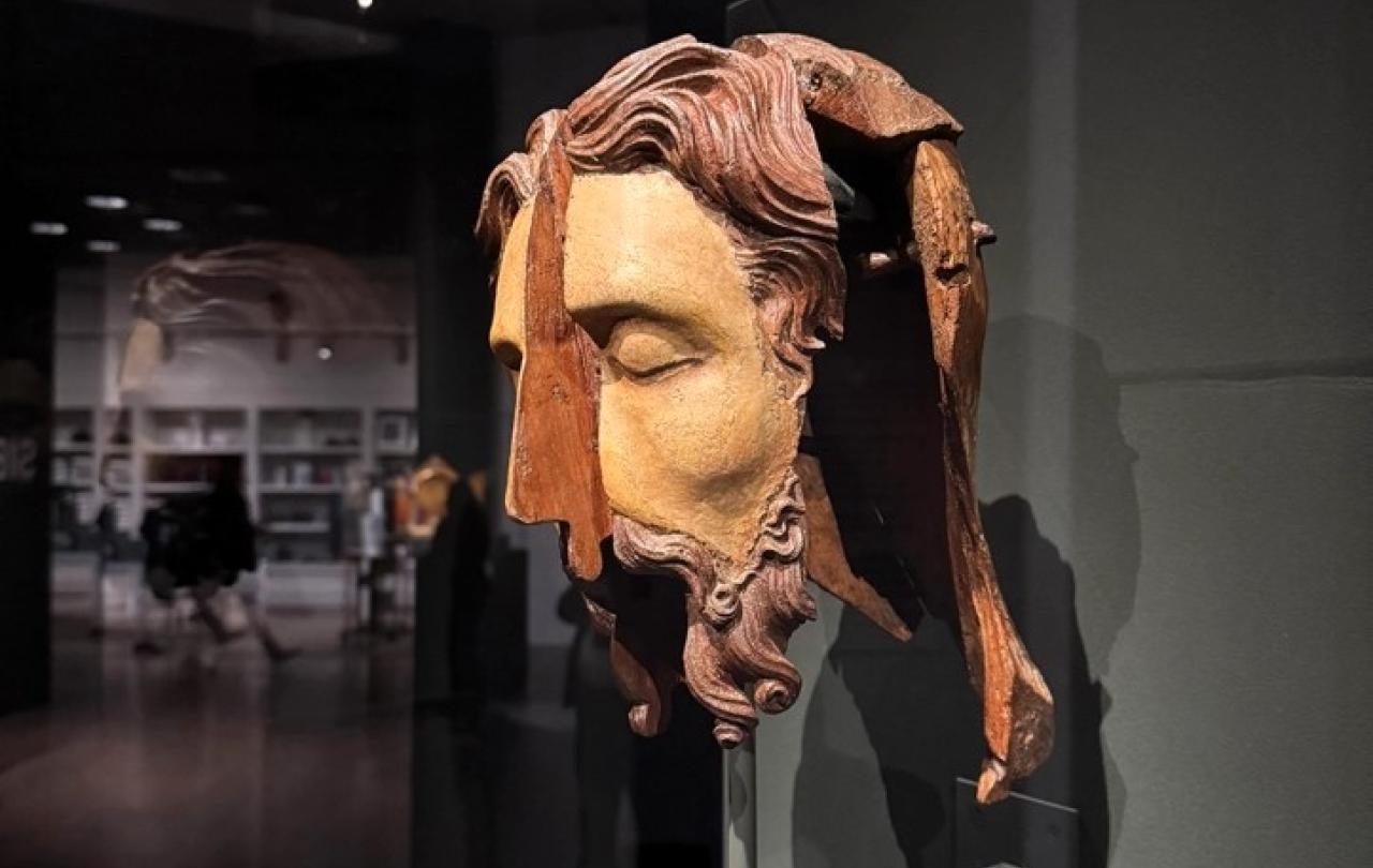 A split wooden sculpted head stands in an exhibition.
