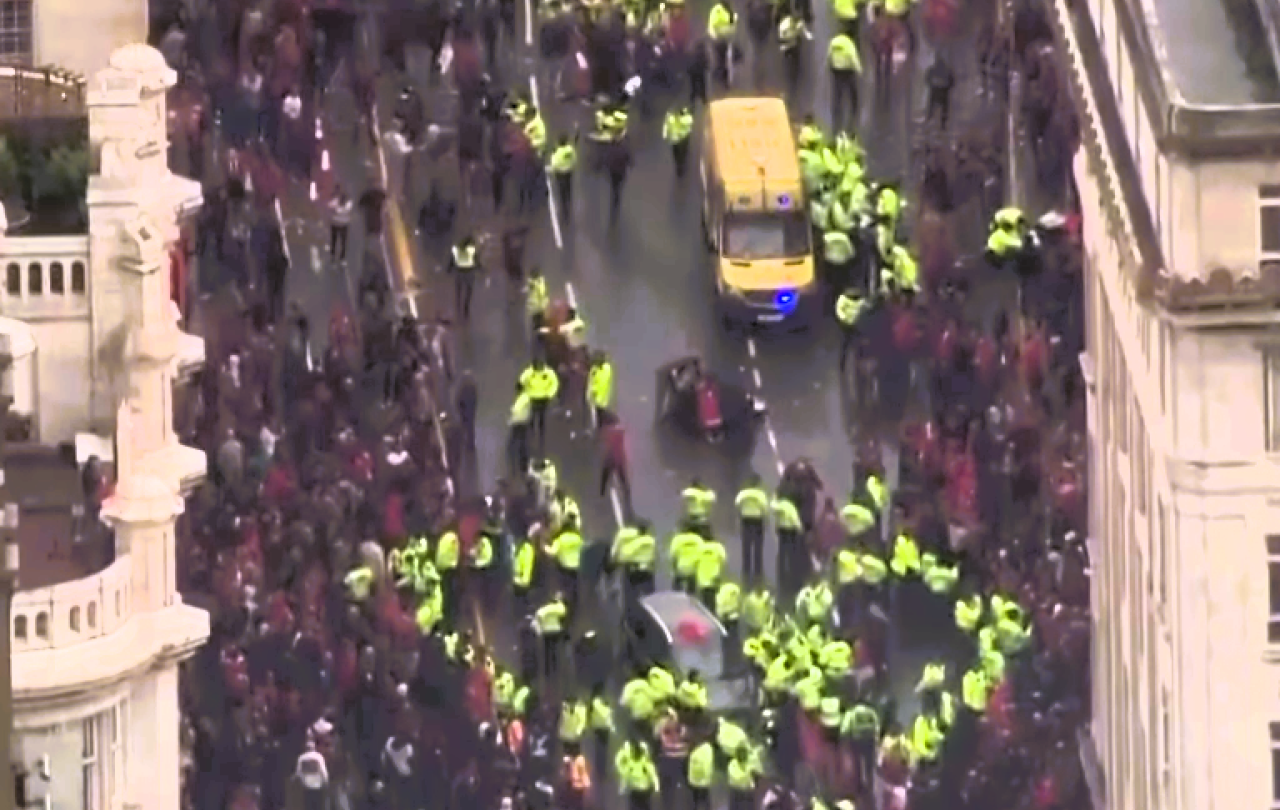 Aerial view of a yellow-jacketed police forming a cordon within a crowd.