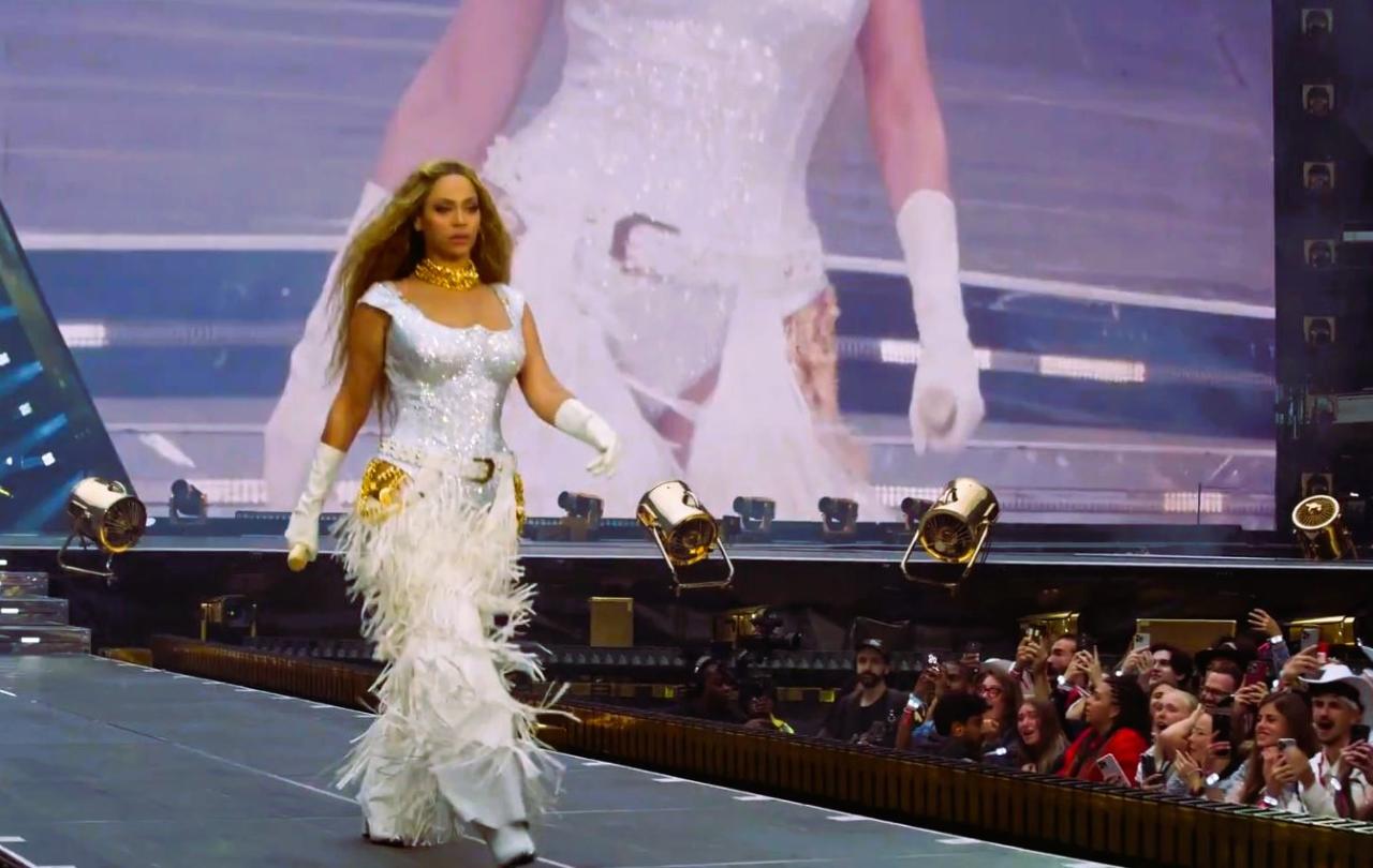 Beyonce marches along a stage catwalk as photographers stare from below.