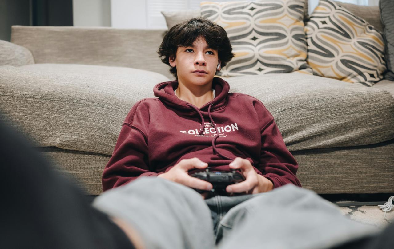 A teenager slumped against a sofa plays a video game