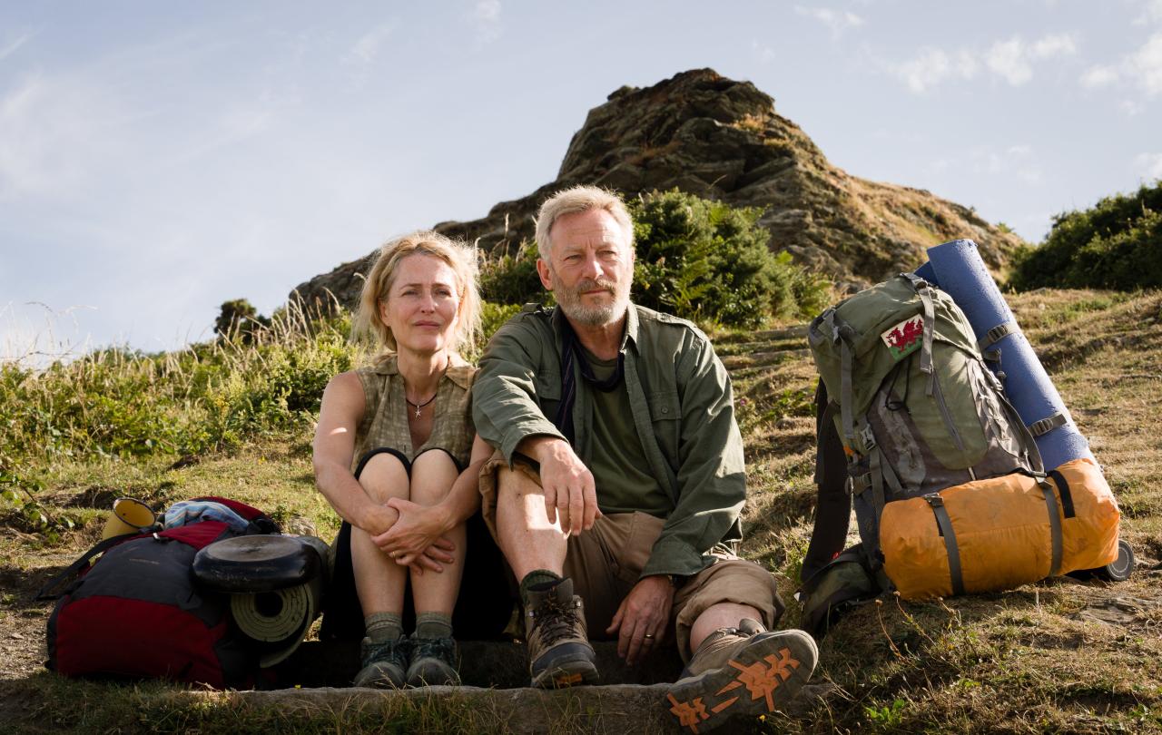 A hiking couple sit on the grass next to a pack.