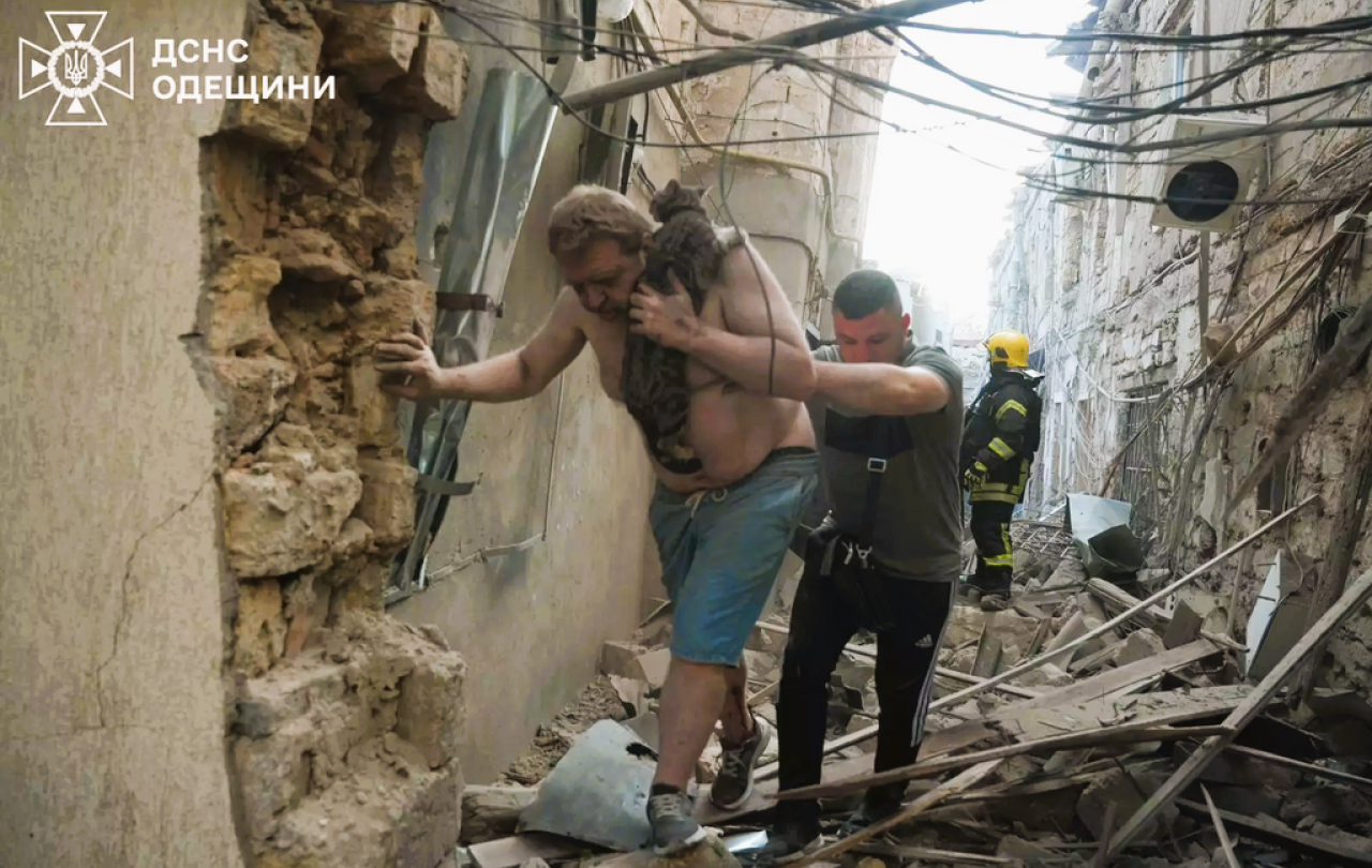 Amid a bombed alley, a victim is helped to walk by a rescue worker