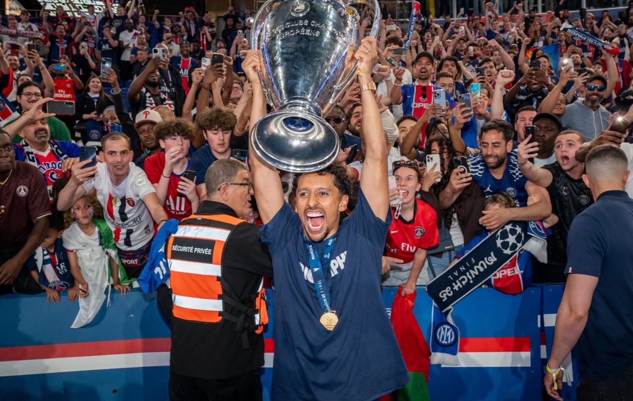 A footballer holds up the European cup, behind him fans are jubillant.