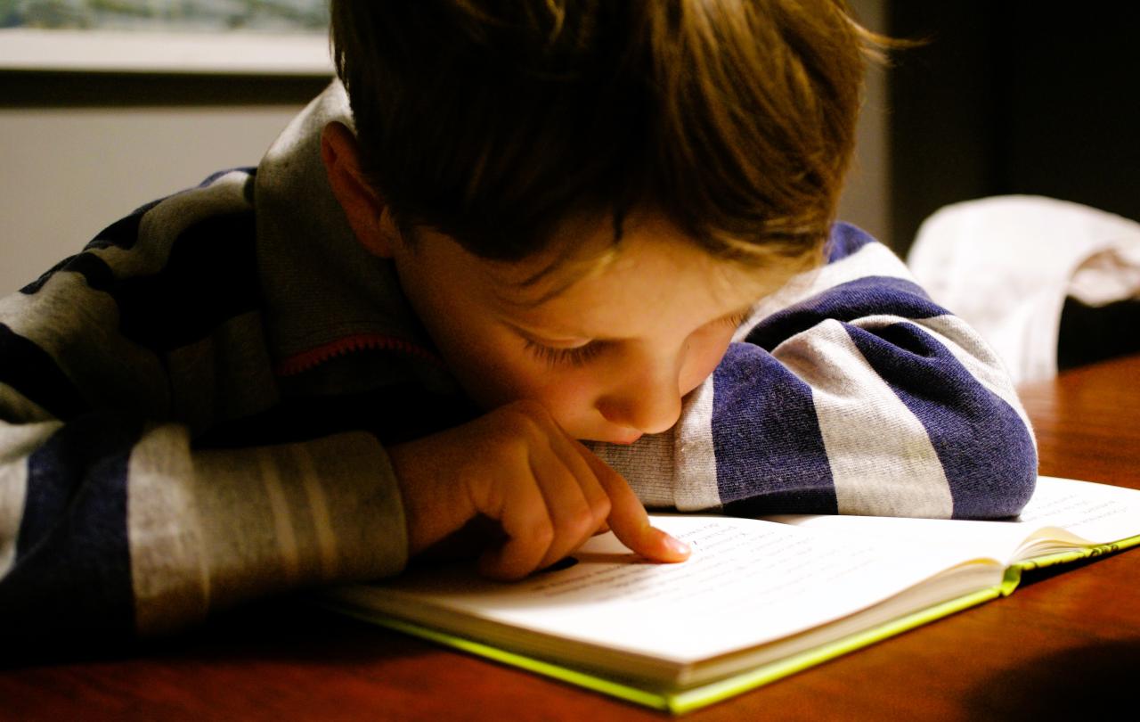 A young boy pores over a book tracing the lines with a finger.
