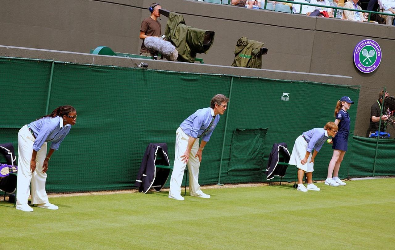 Tennis line judges stand and lean forward with hands on knees