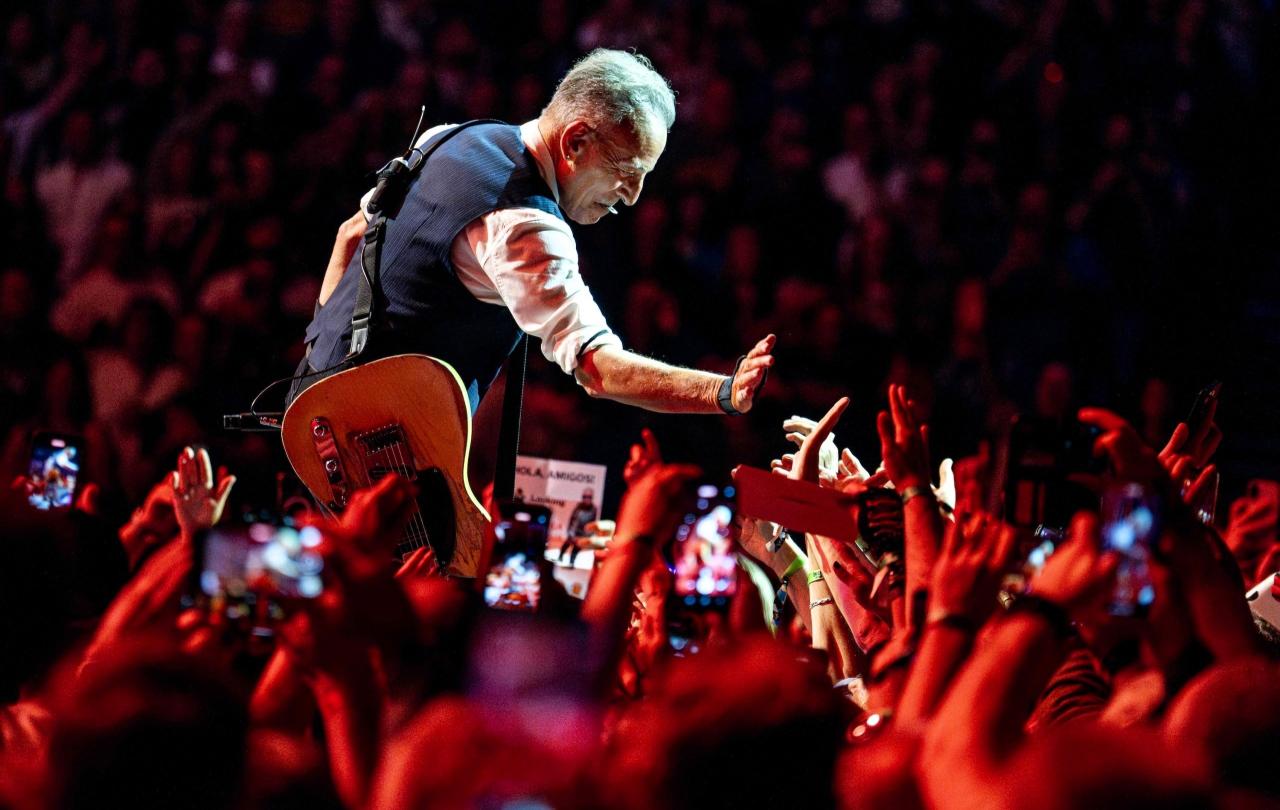 Bruce Springsteen crouches down and holds a hand out to a sea of outstretched hands
