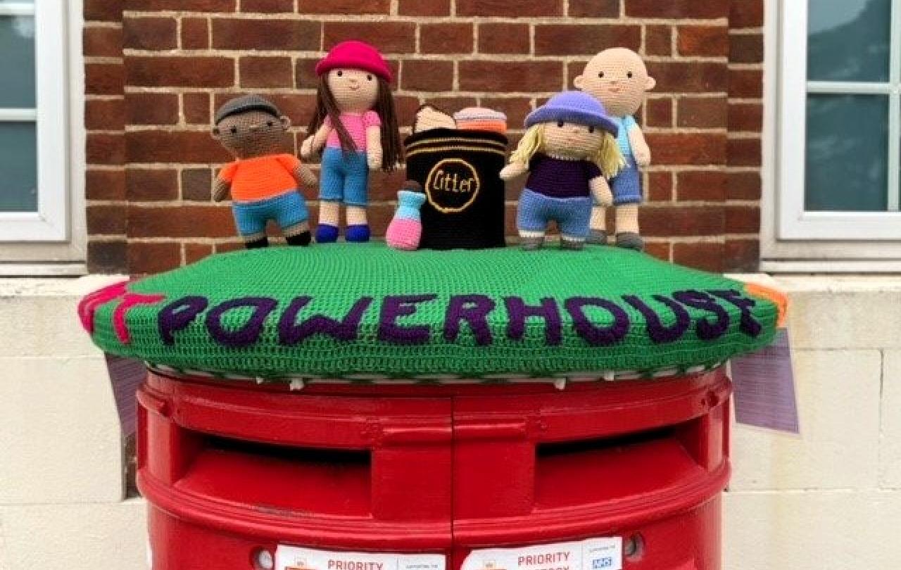 A knitted post box topper shows a group of people and the word powerhouse.