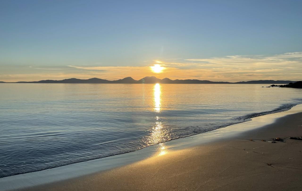A sunset over an island casts golden light on the sea and a beach.