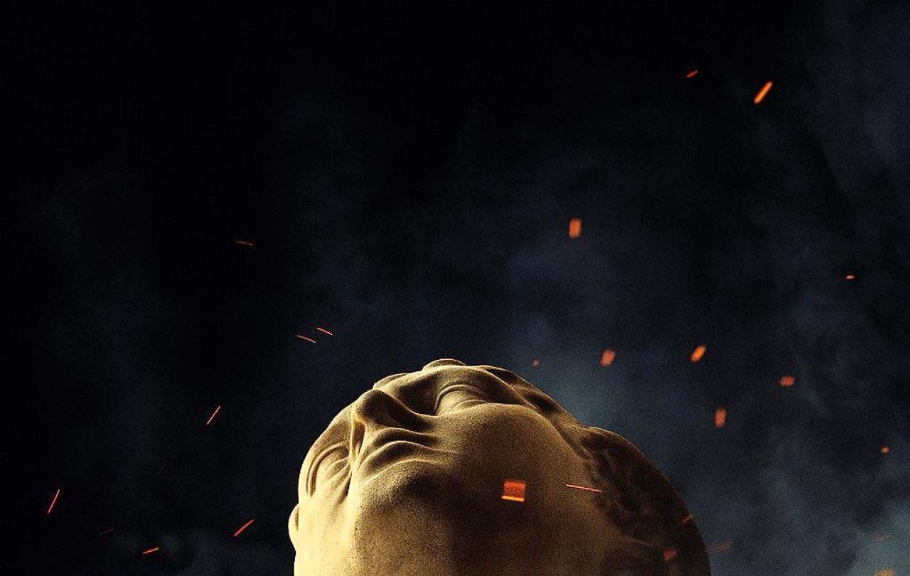 the head of a classical statue looks up amid embers around it.