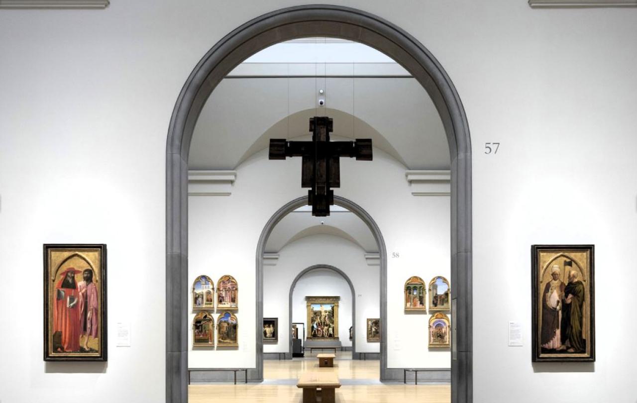 An art gallery arch reveals a suspended crucifix and other paintings in a distant room