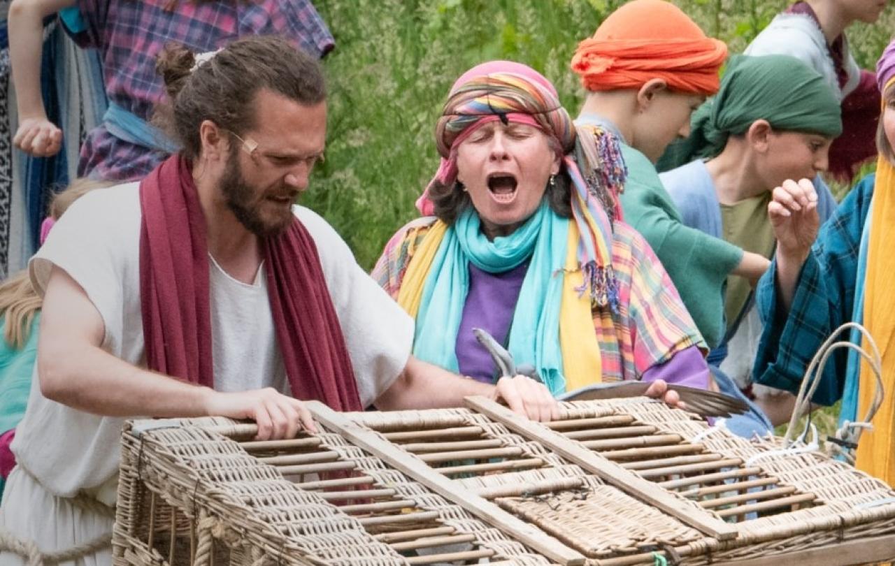 An outdoor theatrical setting shows Jesus with a basket.