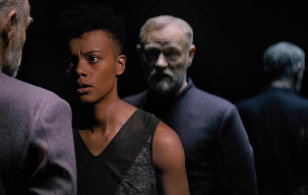 A woman confronts a man whose clone stands behind her.