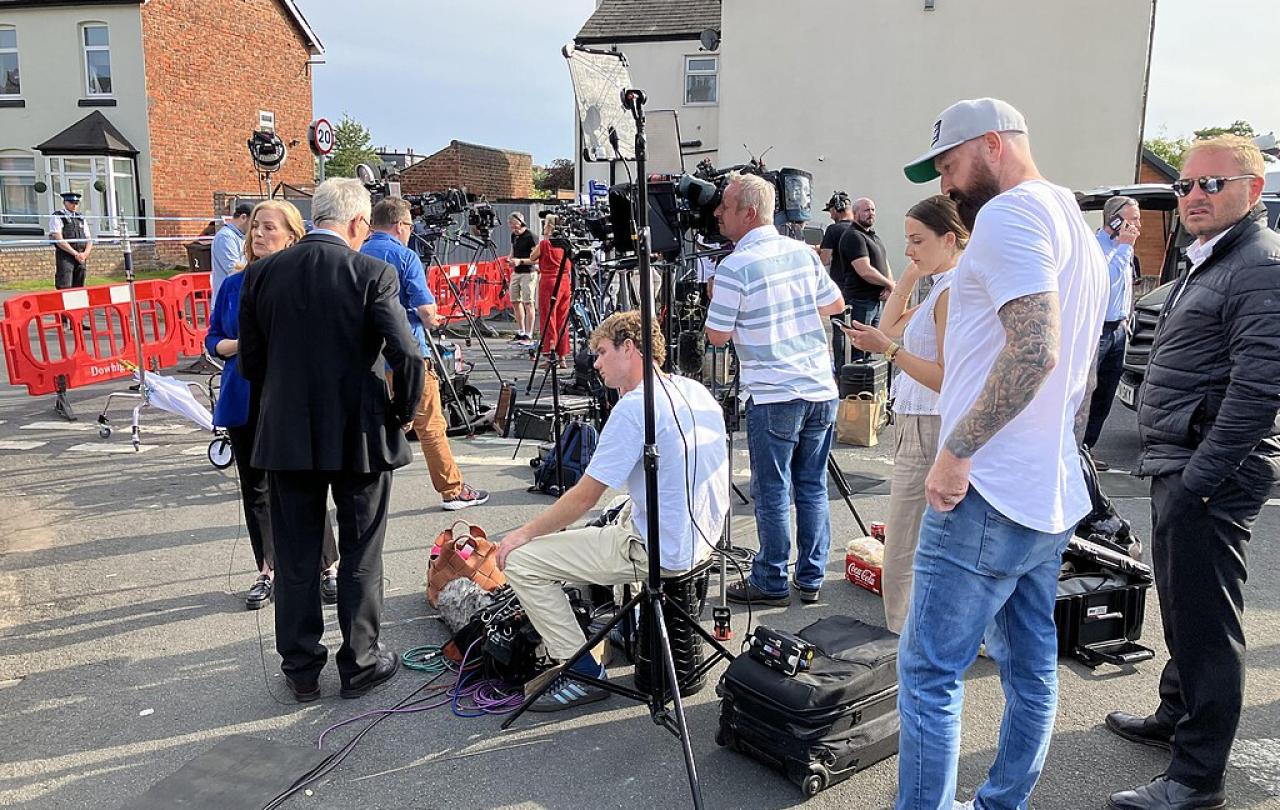 A media pack await a press conference in a street.