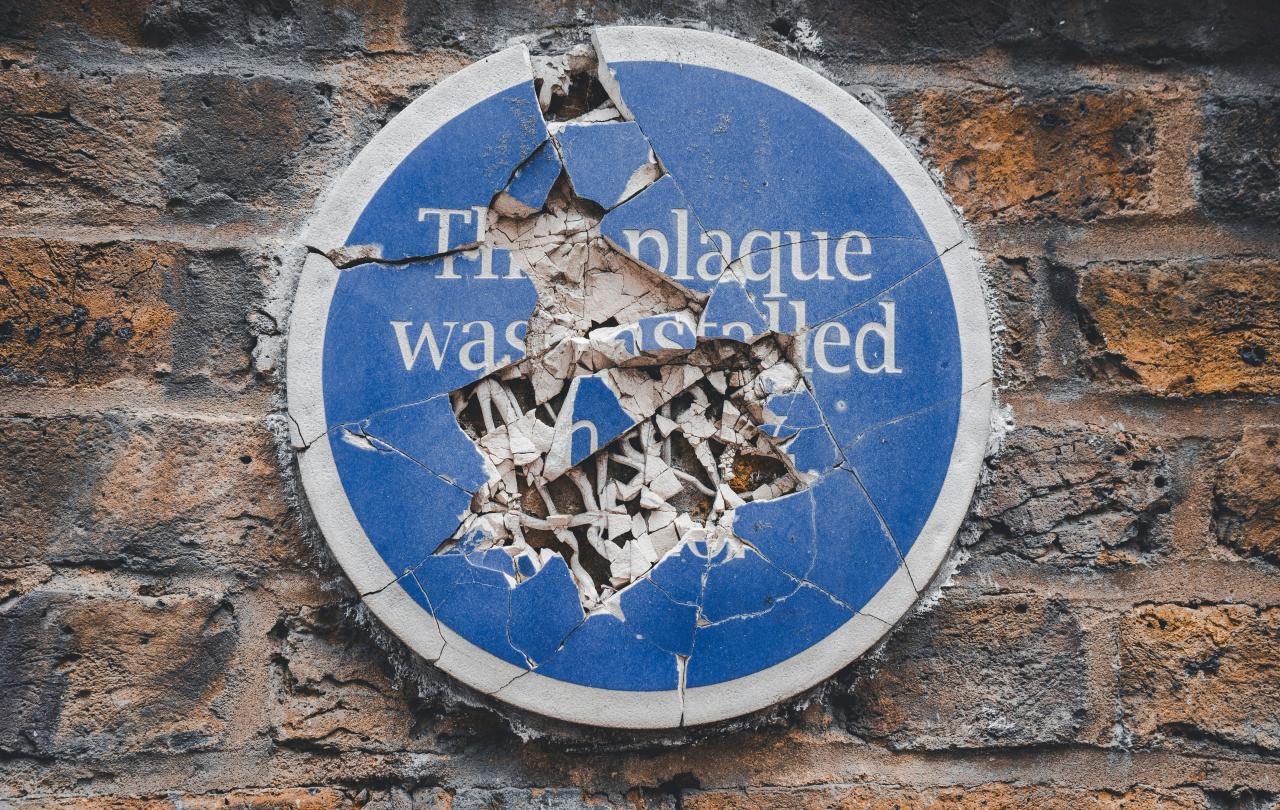 A commemorative blue plaque on a a wall is smashed to pieces