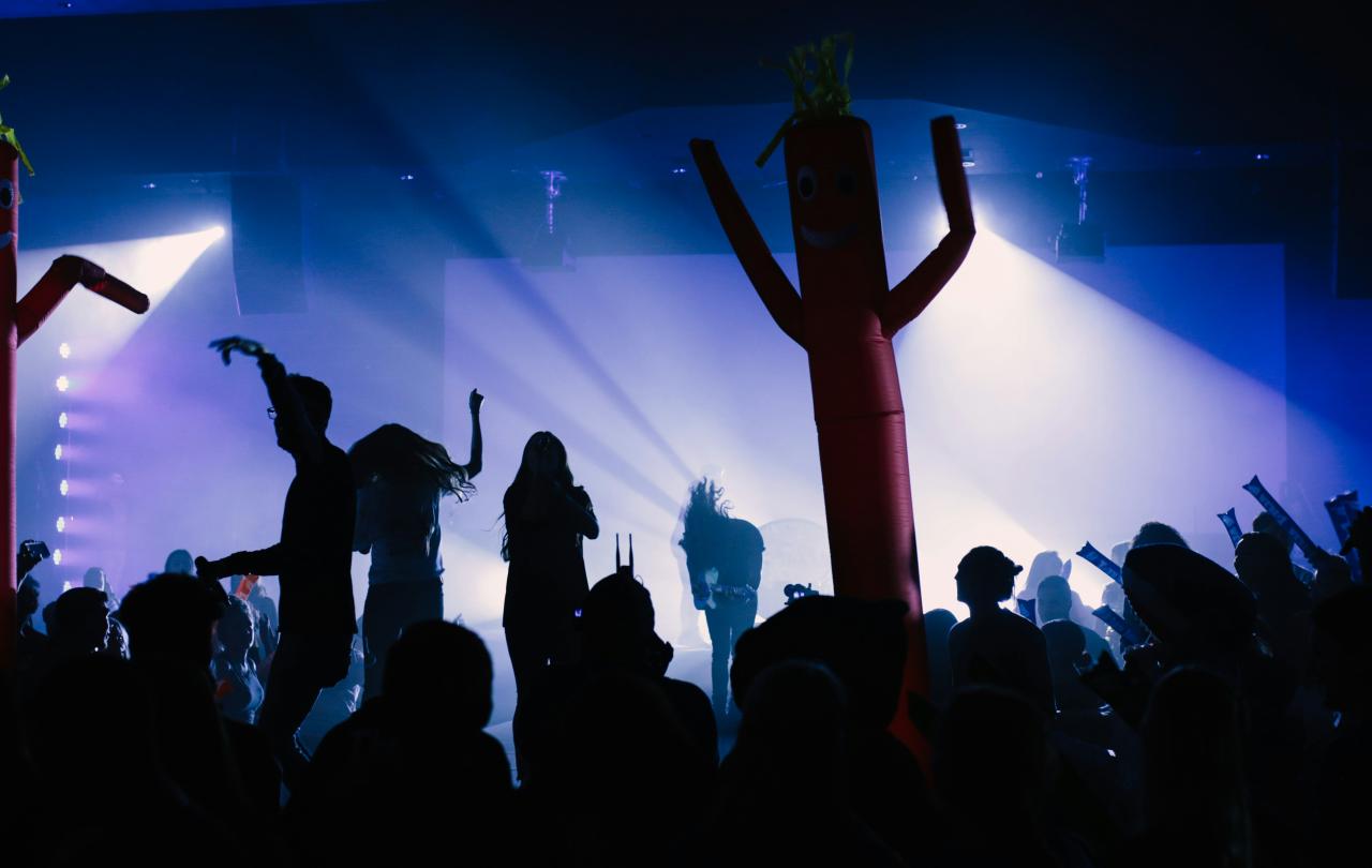 A band and audience are back lit against a stage.
