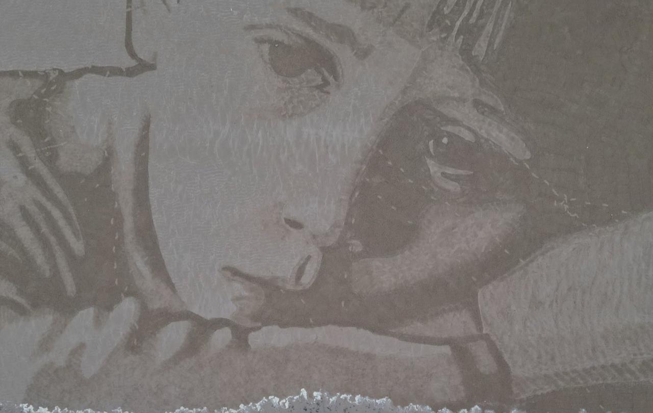 A sand drawing shows an unhappy child's face with the tide coming in from below