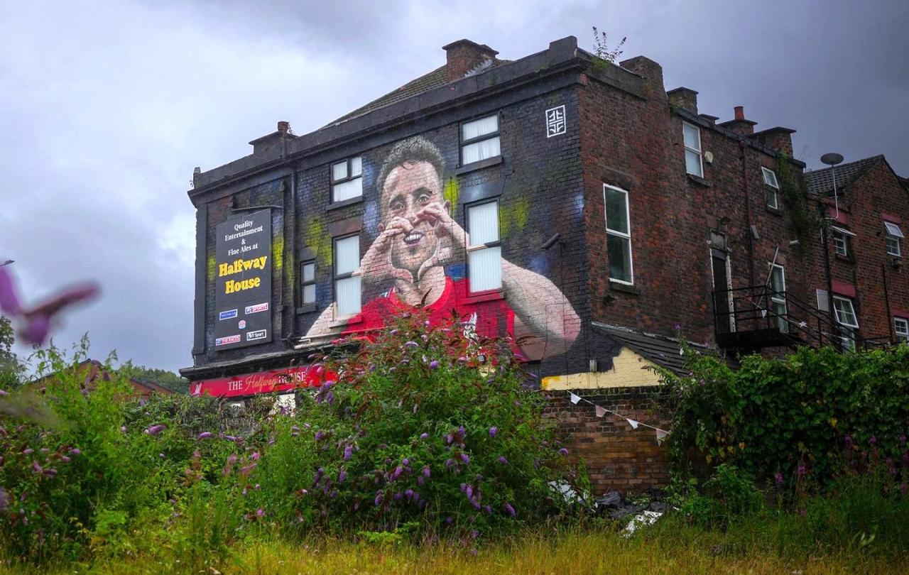 A mural on a side of a pub shows a footballer making a heart sign.