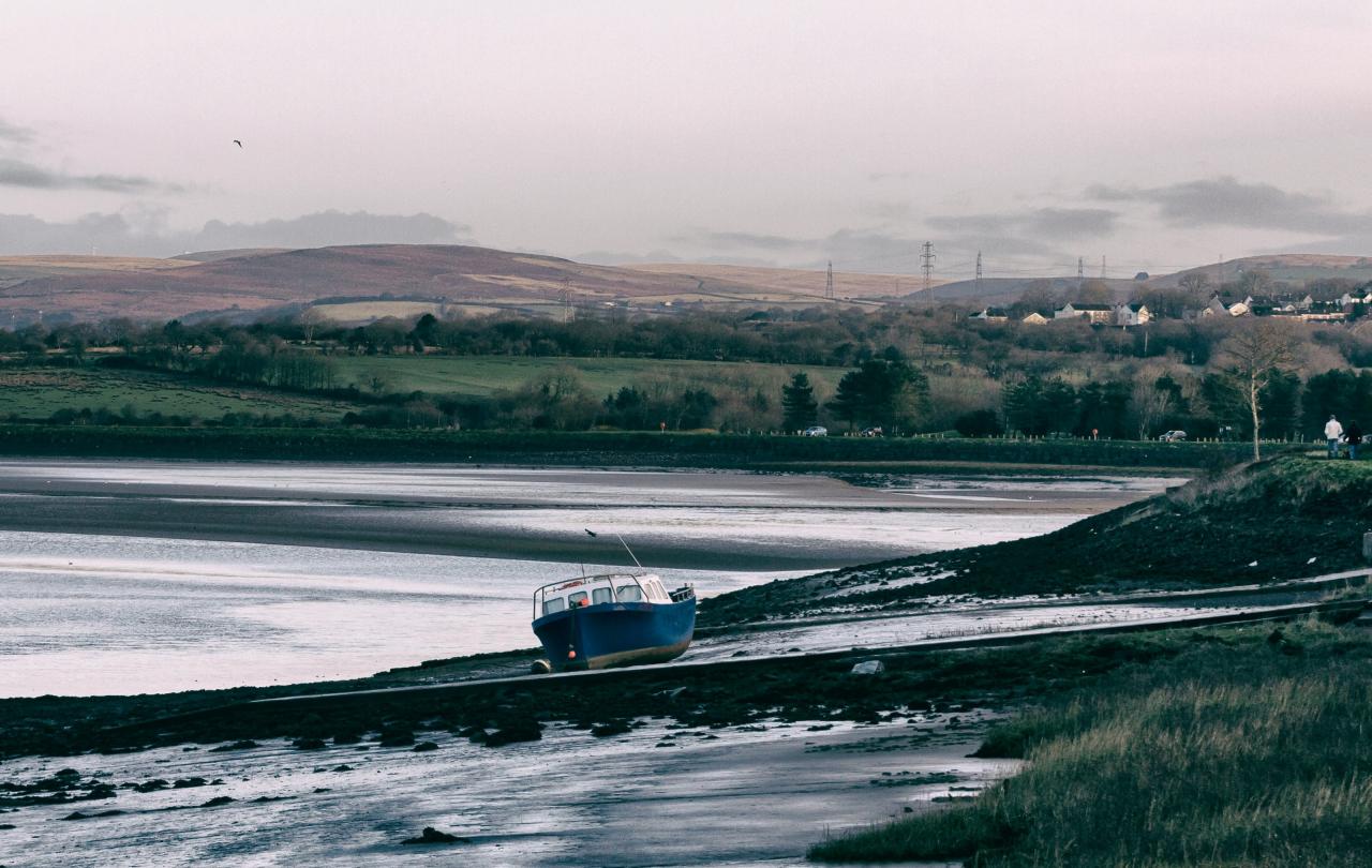 A boat rests on a mud bank of a river, hills are in the background.