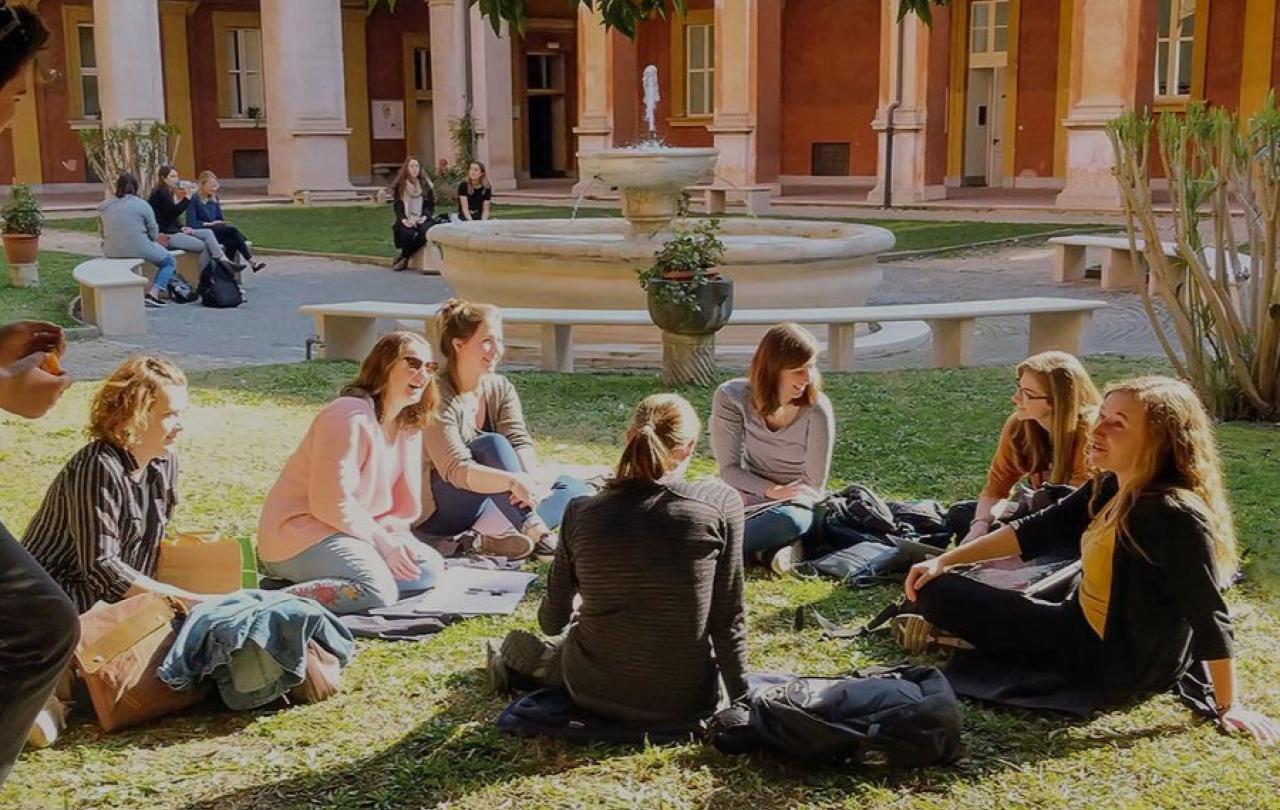 Students sit on the grass in front of a fountain.