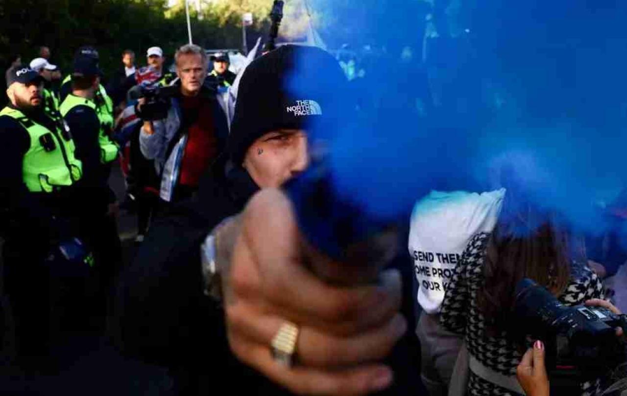 A protestor holds a blue smoke canister towards the camera lens.
