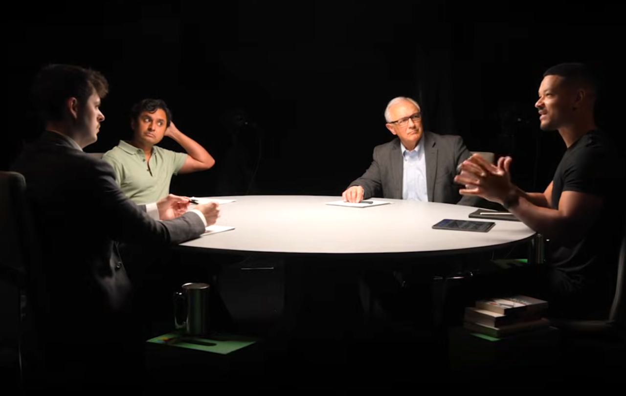 A spotlit round table with podcast guests around it.